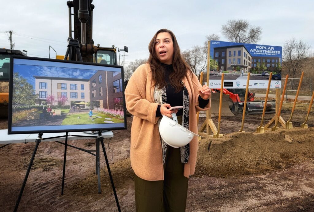 A woman presenting in front of a construction site at a groundbreaking ceremony.