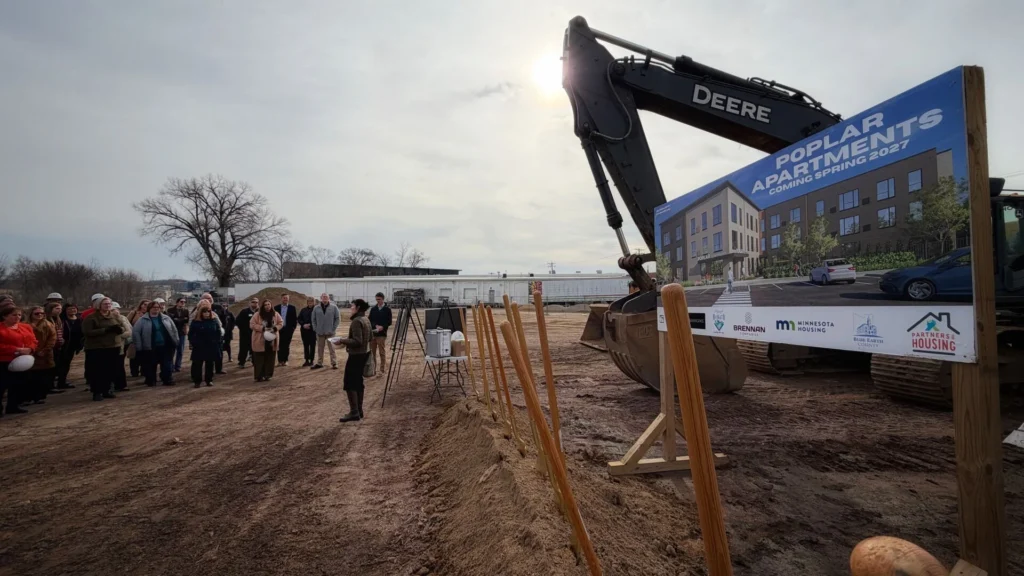 Construction equipment stands ready behind a presenter at a construction site